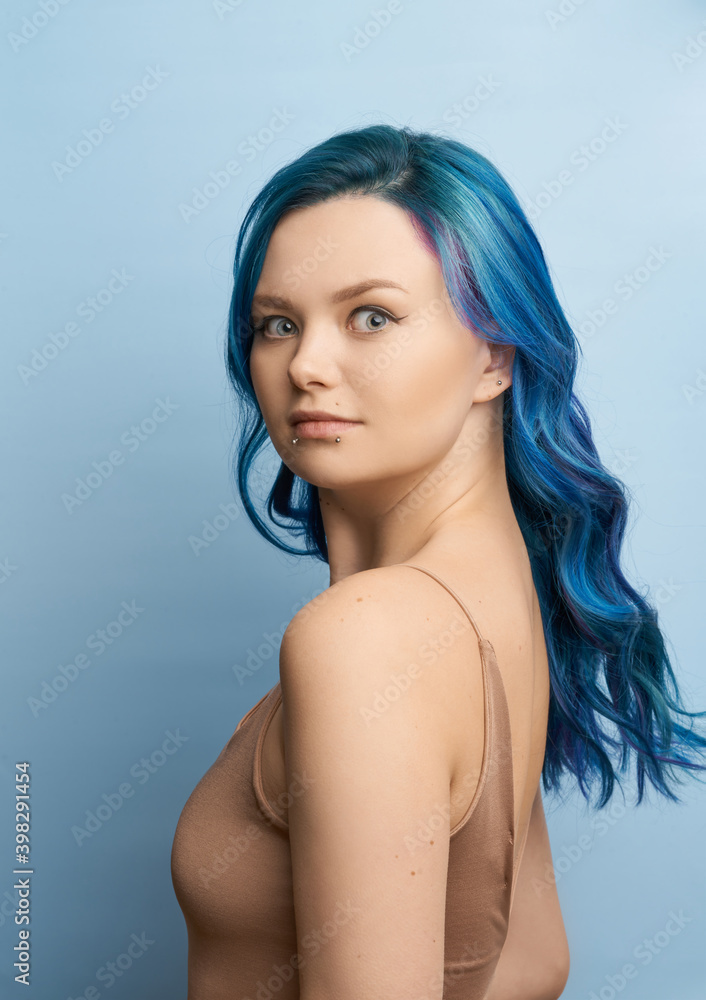 The girl looks in surprise. Advertising discounts concept.. Girl with creative blue coloring and a rainbow in her hair on a blue background. Modern minimalistic bright photography for social networks The girl looks in surprise. Advertising discounts concept.. Girl with creative blue coloring and a rainbow in her hair on a blue background. Modern minimalistic bright photography for social networks