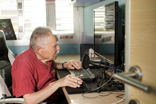 Anziano signore con un paolo è seduto di fronte al computer mentre di una camerata mentre utilizza il mouse  photo