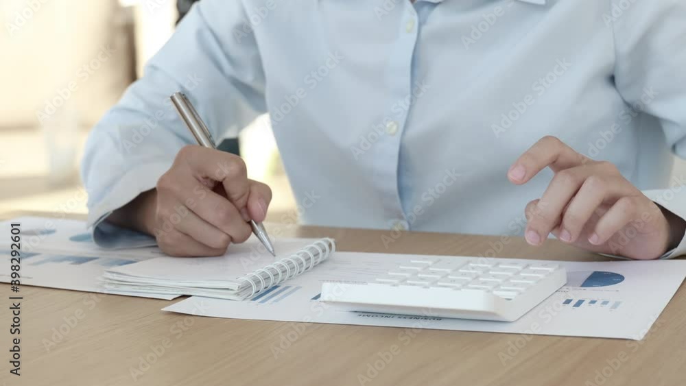 Young Asian woman presses a calculator and takes notes in her office. Young Asian woman presses a calculator and takes notes in her office.