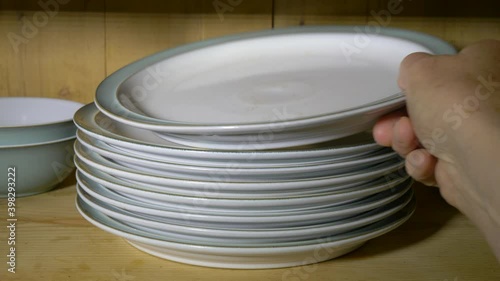 Closeup POV shot of a man’s hand opening the door of an old glass fronted, pine kitchen wall cupboard, putting two dinner plates back onto their pile, then closing the door.