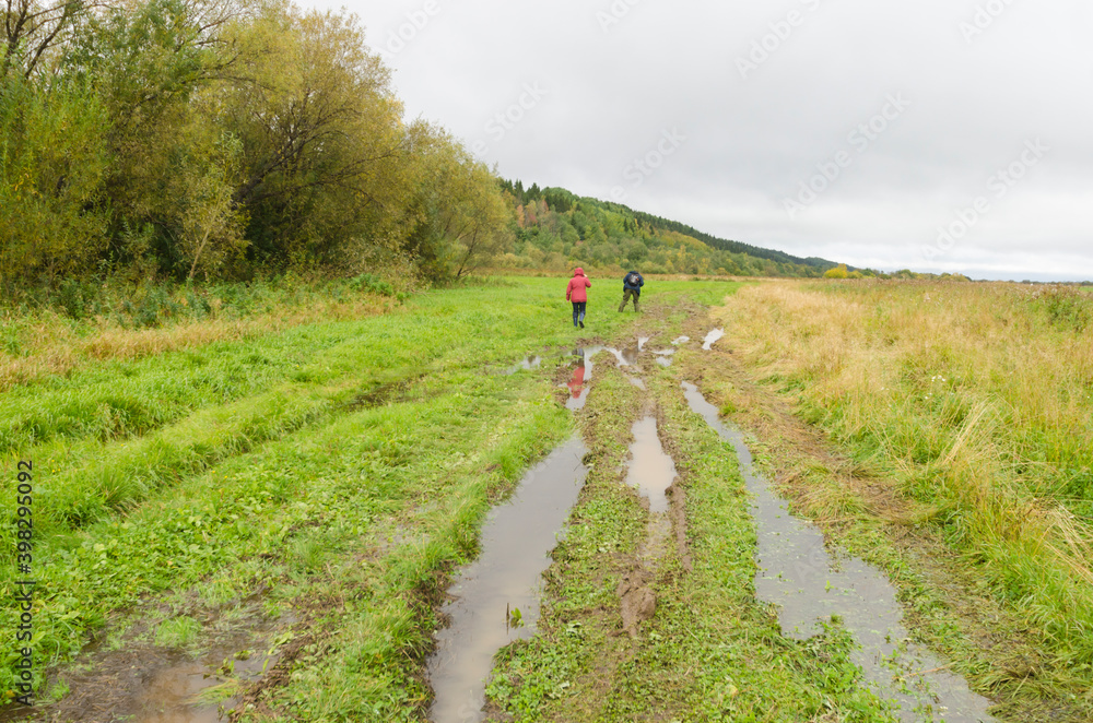 Two travelers are walking along a green field and a dirt road. Family travel