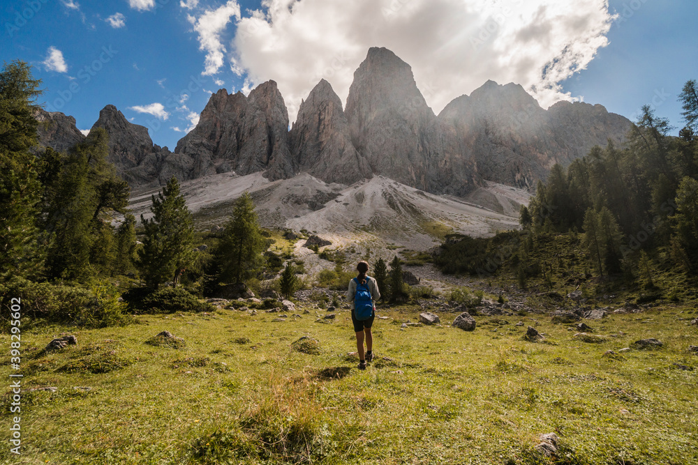Young girl hiker with the back at the camera looking towards the cliffs in Dolomites, Italy.