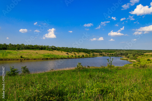 Summer landscape with beautiful lake, green meadows, hills, trees and blue sky