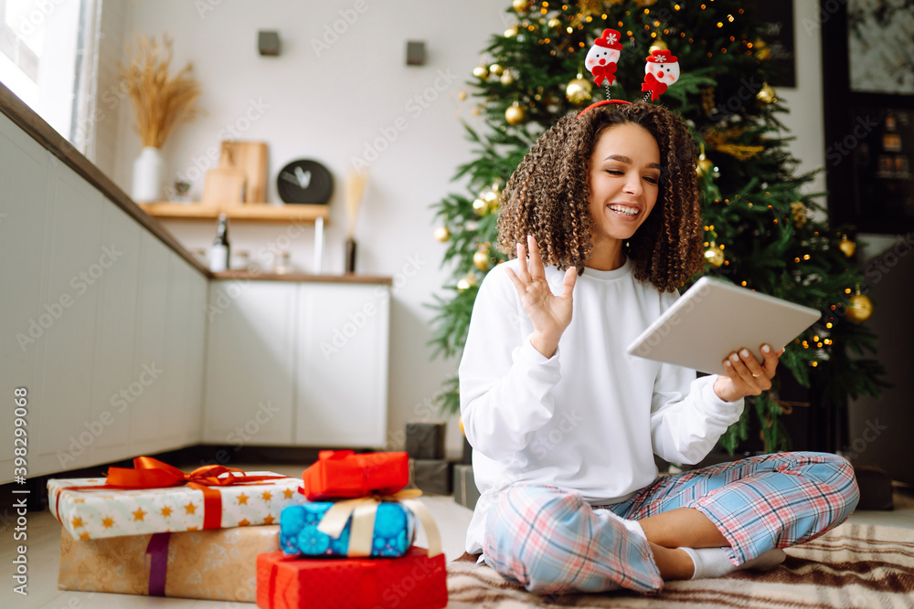 Christmas online holiday. Happy woman having video call with their family or friends. Young woman uses a digital tablet near decorated festive tree at home. Virtual meeting. Covid-2019. Christmas online holiday. Happy woman having video call with their family or friends. Young woman uses a digital tablet near decorated festive tree at home. Virtual meeting. Covid-2019.