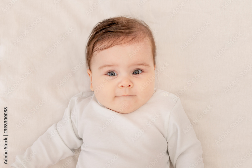 cute baby six months lying in a crib in a white bodysuit
