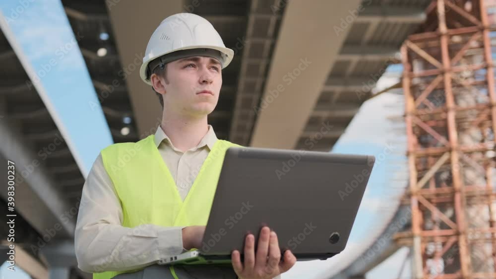 young engineer in helmet and vest on construction site working on laptop. young engineer in helmet and vest on construction site working on laptop.