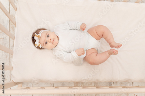 baby six months in bed with a bottle of water in a white bodysuit