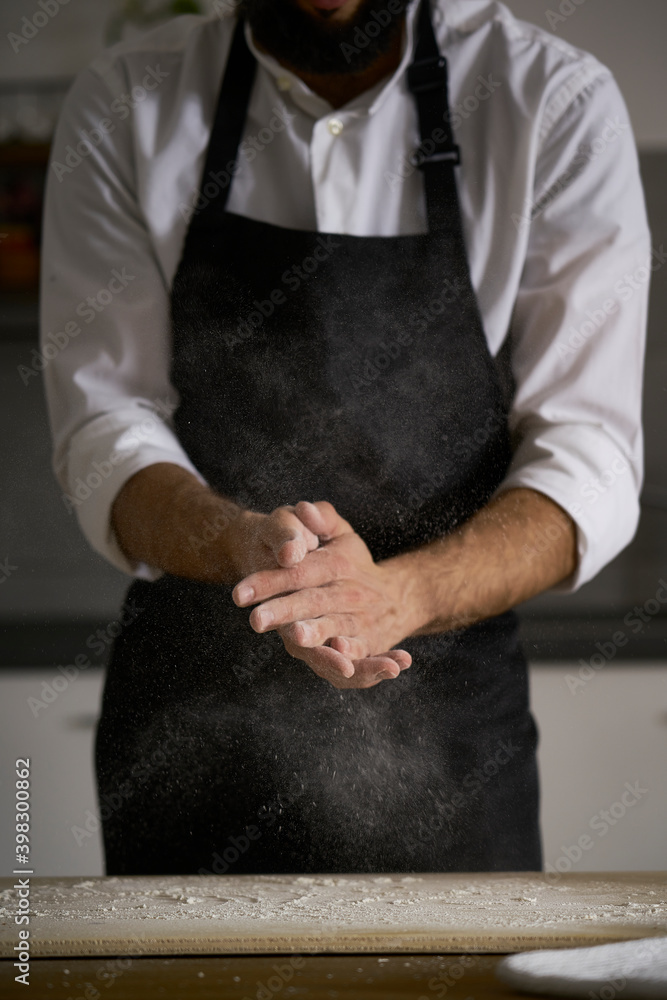 The hands of the strong man knead the dough from which they will make bread, pasta, cake or pizza. In his kitchen he carries on the tradition of homemade pasta. A cloud of white flour flies like dust.