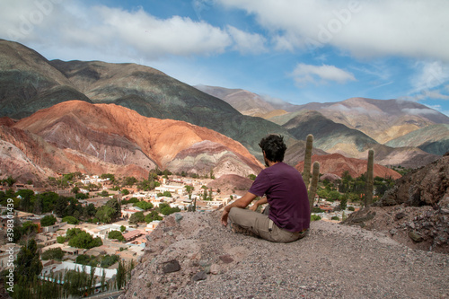 Man sitting in the mountains, looking at the town of Purmamarca. 