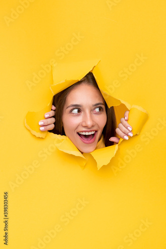 Fototapeta Excited woman through torn paper hole