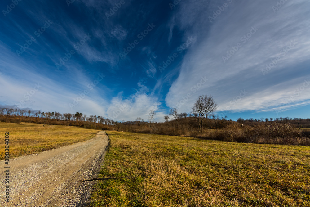 dirt road and a hill with forest and fine clouds at the sky