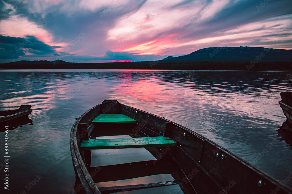 wooden boat on the shore of the lake after sunset with purple clouds