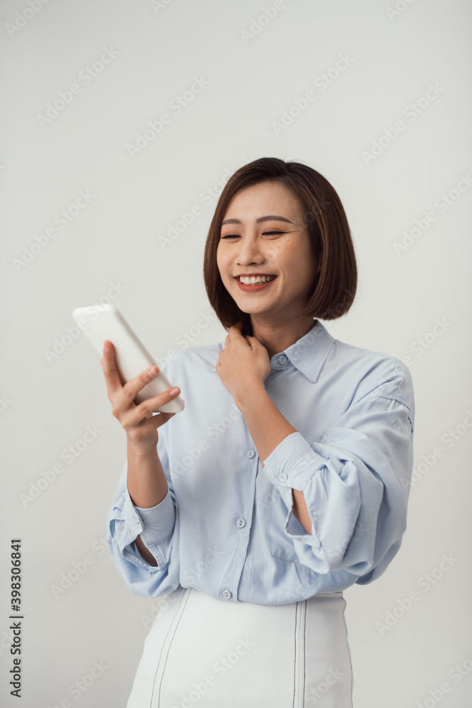 Image of satisfied asian woman smiling and looking at cell phone holding in hand isolated over white background Image of satisfied asian woman smiling and looking at cell phone holding in hand isolated over white background