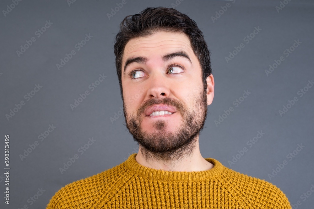 Obraz premium Amazed Young handsome Caucasian man wearing yellow sweater against gray wall bitting lip and looking tricky to empty space.