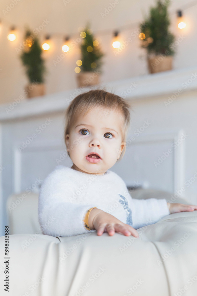 Baby on sofa near christmas tree is smiles so that two teeth are visible Baby on sofa near christmas tree is smiles so that two teeth are visible