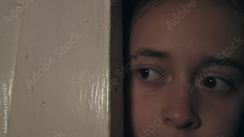 A teenage girl looks out of the door to check what is happening outside.