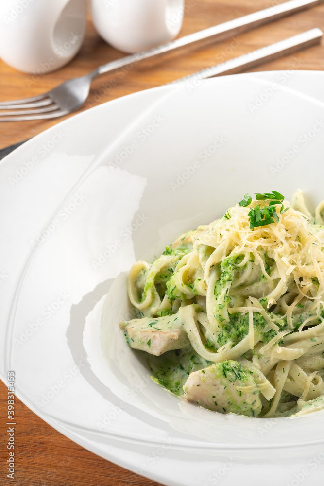 Tagliatelle pasta with pesto, chicken and Parmesan in a white plate on a wooden table, close up