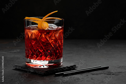 Classic Negroni Cocktail in a retro glass with ice and orange peel on a black background, space for text