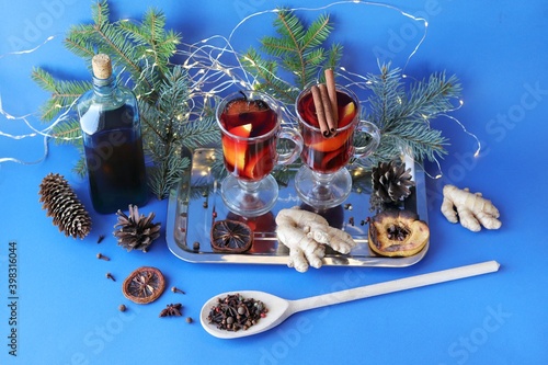 Fototapeta Naklejka Na Ścianę i Meble -  Traditional Christmas drink, cups with mulled wine, spices, fir branches and illumination on a dark background, the concept of home comfort, winter holidays celebration