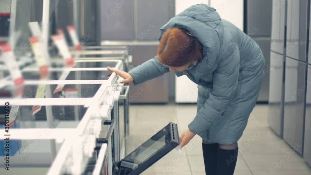 a woman chooses an induction cooker for the kitchen in a home appliance hypermarket a woman chooses an induction cooker for the kitchen in a home appliance hypermarket