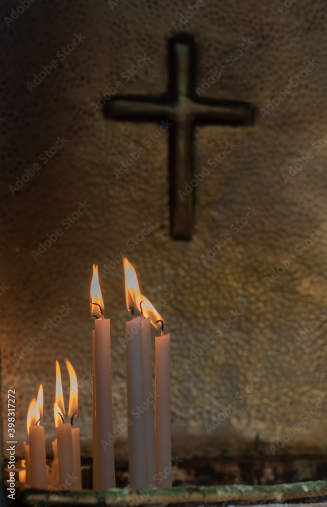 burning candles and a cross in the background, candles lit inside the Church
