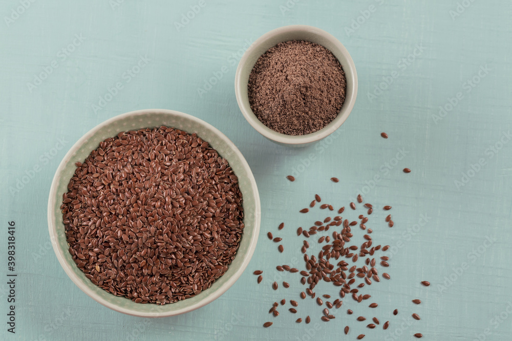 Brown flax seed and ground or crushed flaxseed or linseed in small bowl on a light blue background. Brown flax seed and ground or crushed flaxseed or linseed in small bowl on a light blue background.