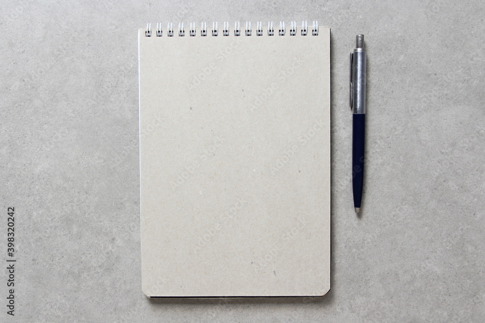 A spring notebook with a sheet of craft paper A5 with a ballpoint pen on light grey concrete background. Concept of new idea, business plan and strategy. Empty space for text A spring notebook with a sheet of craft paper A5 with a ballpoint pen on light grey concrete background. Concept of new idea, business plan and strategy. Empty space for text
