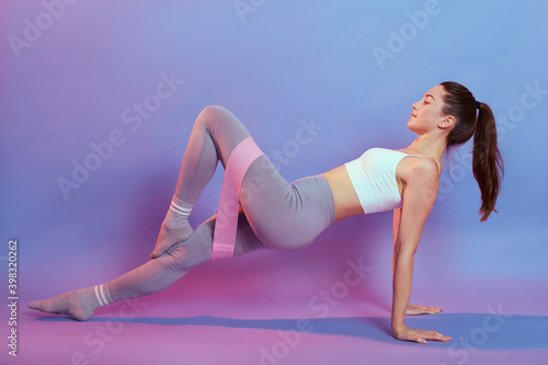 Slim fitness woman stretching body in upward plank pose, doing reverse planking exercise with resistance elastic band indoor, female strength training her core with bodyweight, flexibility exercises.