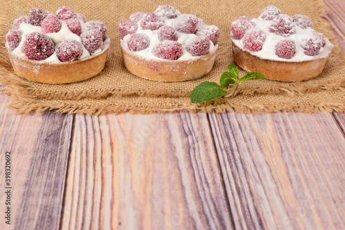 Side view of raspberry tartlets lying on a matting on a wooden table.