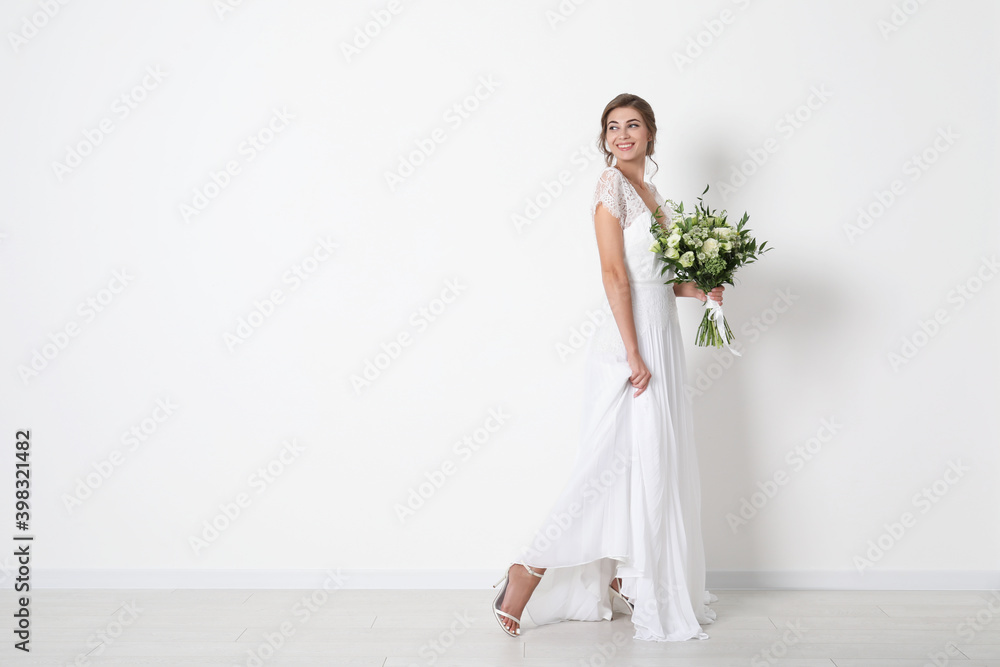 Young bride wearing wedding dress with beautiful bouquet near light wall. Space for text Young bride wearing wedding dress with beautiful bouquet near light wall. Space for text