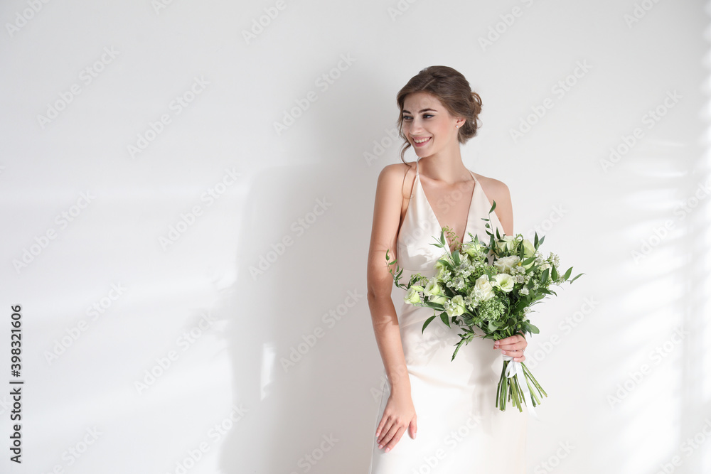 Young bride wearing wedding dress with beautiful bouquet on light background. Space for text Young bride wearing wedding dress with beautiful bouquet on light background. Space for text
