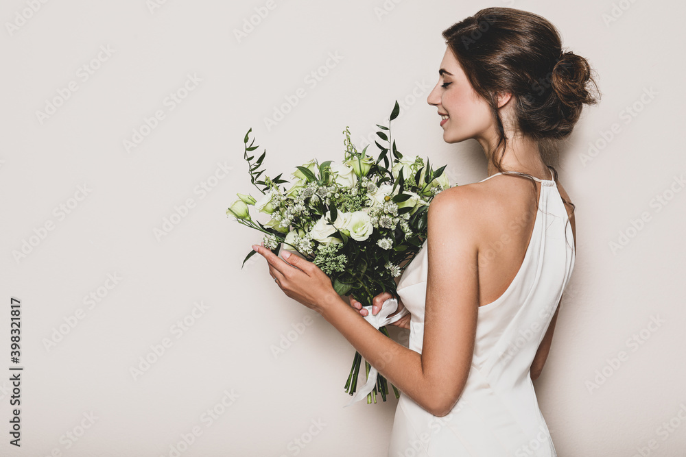 Young bride wearing wedding dress with beautiful bouquet on beige background Young bride wearing wedding dress with beautiful bouquet on beige background