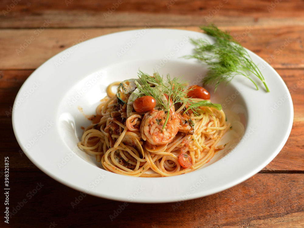 Italian seafood pasta pescatore served in a white plate on a rustic wooden table, selective focus