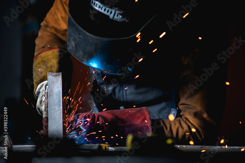 Selective focus of welder in mask and gloves working with metal profile on dark background 