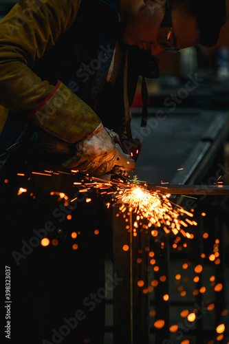 Selective focus of locksmith in goggles and glove working with angle grinder in factory 