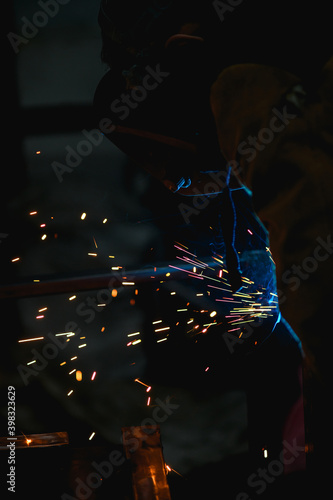 Welder working with sparkling welding in dark workshop 