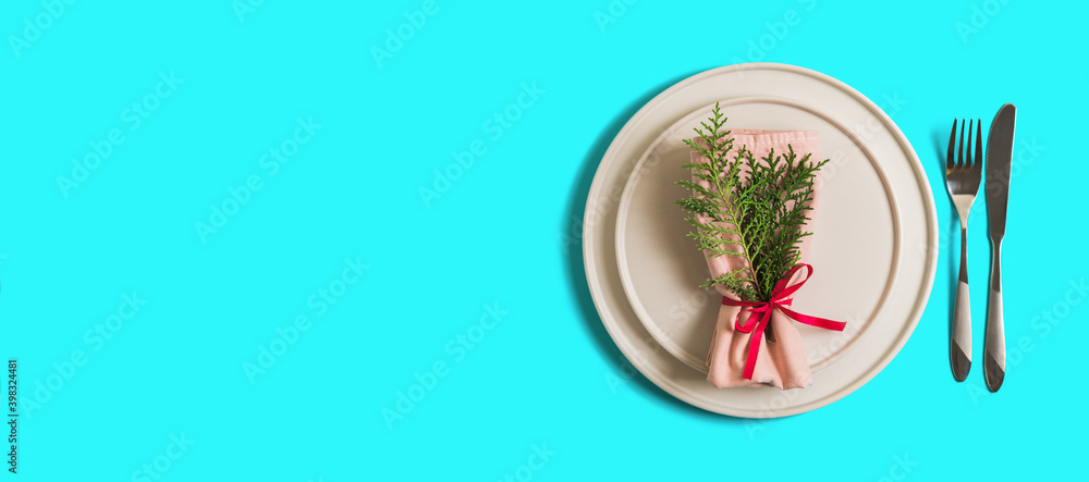 Banner with served table with empty plate and cutlery for celebration of Christmas and New Year. On plate is napkin with Christmas tree branch. Flatlay banner on bright blue background. Top view. Banner with served table with empty plate and cutlery for celebration of Christmas and New Year. On plate is napkin with Christmas tree branch. Flatlay banner on bright blue background. Top view.