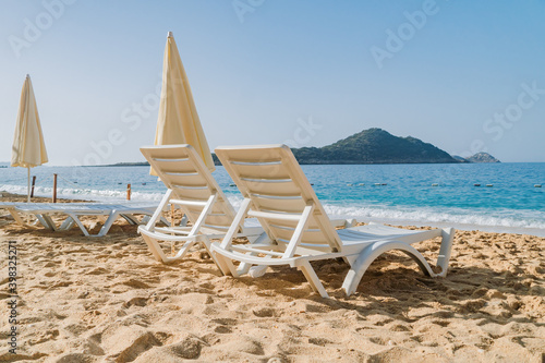 Empty Beach chairs and a yellow sun umbrella await tourists against the backdrop of the blue sea. Beautiful seashore beach resort.