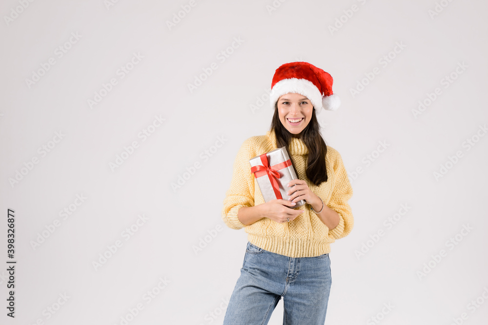 Happy excited young woman in santa claus hat with gift box over gray background Happy excited young woman in santa claus hat with gift box over gray background