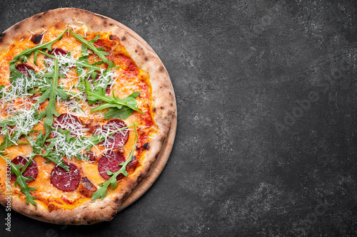 Pizza with cheese, sausage and arugula, on a wooden board, on a dark background