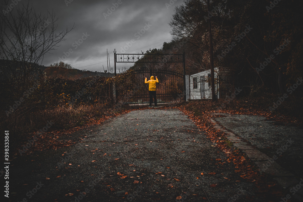 Man dressed with yellow waterproof and standing in front of shut old metal gate, shot near by Kavarna town, Bulgaria, in the first half of December 2020