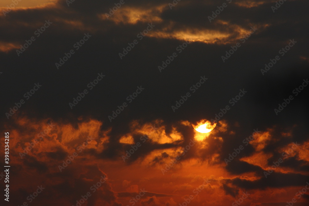 słońce na pochmurnym ciemnopomarańczowym niebie, częściowo zasłonięte przez czarne chmury