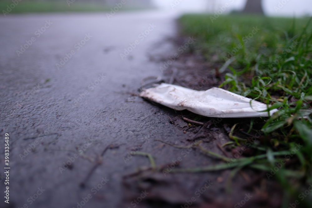 White protective fask mask discarded on the floor in a public park, new environmental issue arises as people throw away face masks in public creating rubbish White protective fask mask discarded on the floor in a public park, new environmental issue arises as people throw away face masks in public creating rubbish