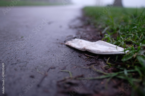 White protective fask mask discarded on the floor in a public park, new environmental issue arises as people throw away face masks in public creating rubbish