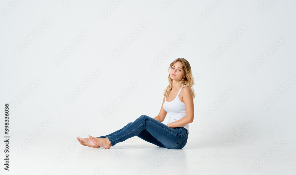 a woman sits on the floor on a light background in jeans and a t-shirt side view 