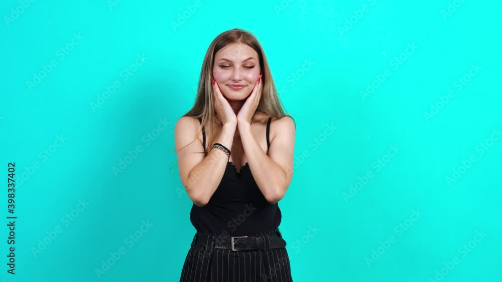 The teenager in love makes the sign of the heart with her hands. Charming girl, dressed in black T-shirt with cleavage, in the studio on a blue background. female casting for TV commercial, student The teenager in love makes the sign of the heart with her hands. Charming girl, dressed in black T-shirt with cleavage, in the studio on a blue background. female casting for TV commercial, student
