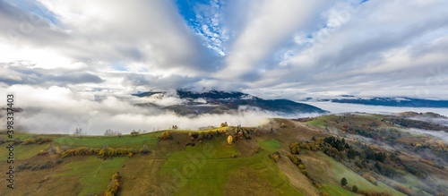 Fly over landscapes of green hills under a layer of white and fluffy clouds