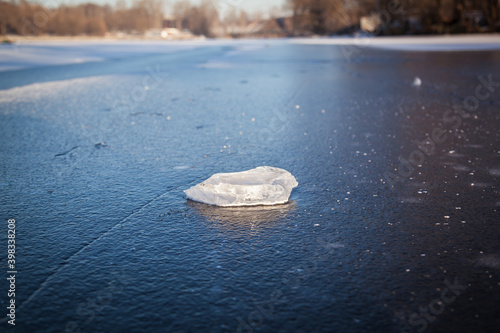 A piece of ice lies on the frozen water of the reservoir, melts and sparkles in the sun. Hard snow with a surface crust.