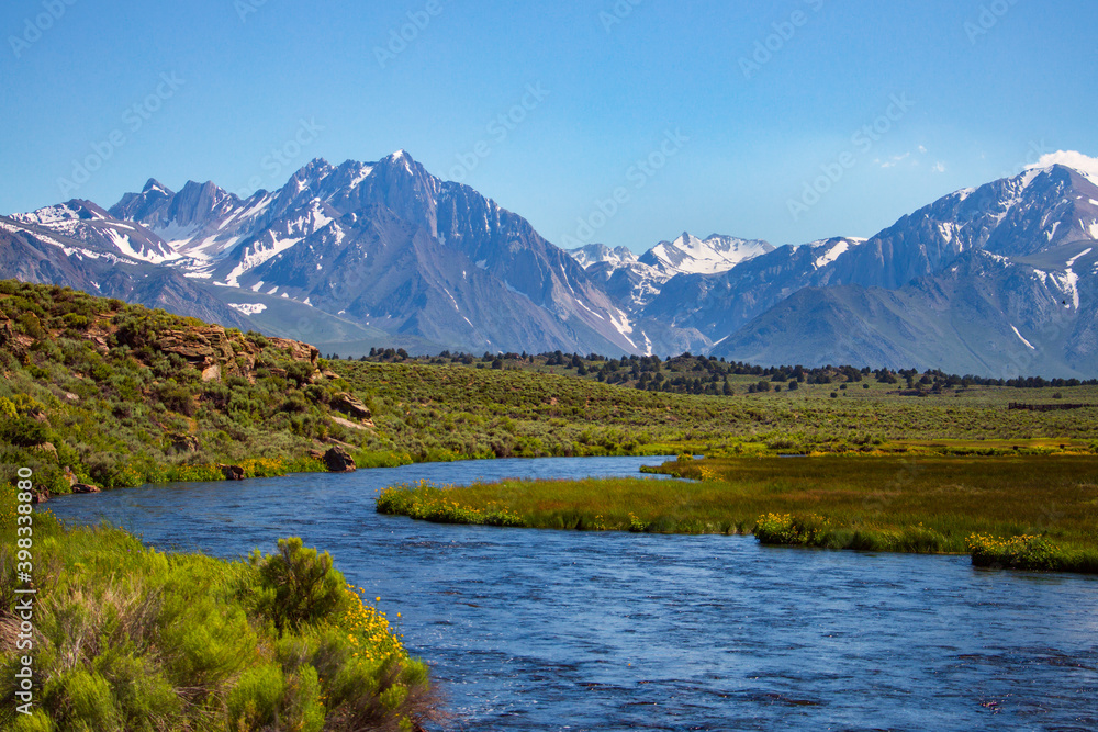 A stream running through a meadow with snowy mountains