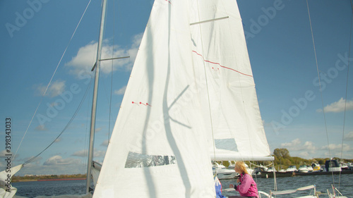 Blonde girl in pink jacket sitting on the stern of a yacht, white sail and yacht blue sky background. Slow motion © iaginzburg